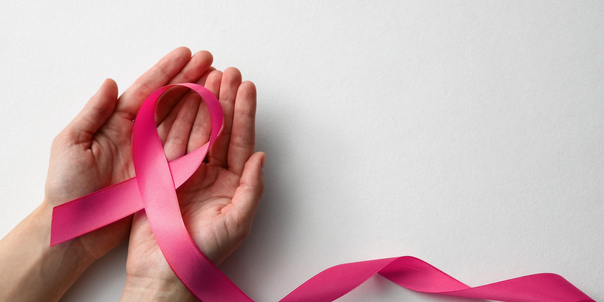 Woman holding pink ribbon on white background, top view with space for text. Breast cancer awareness concept